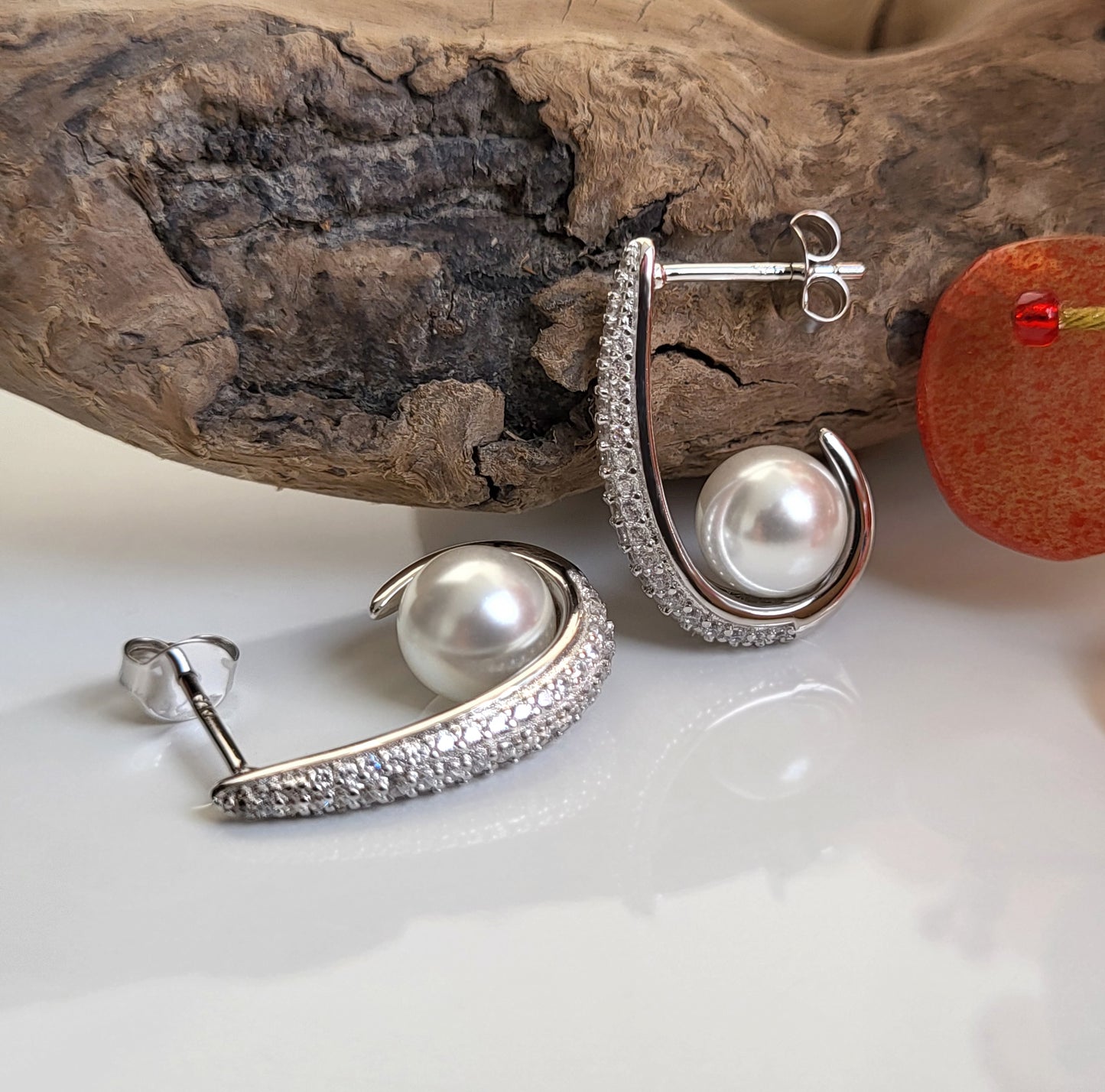 Geschwungene Silberohrringe mit Zirkonia und Perle mit Lineal in liegender Ansicht