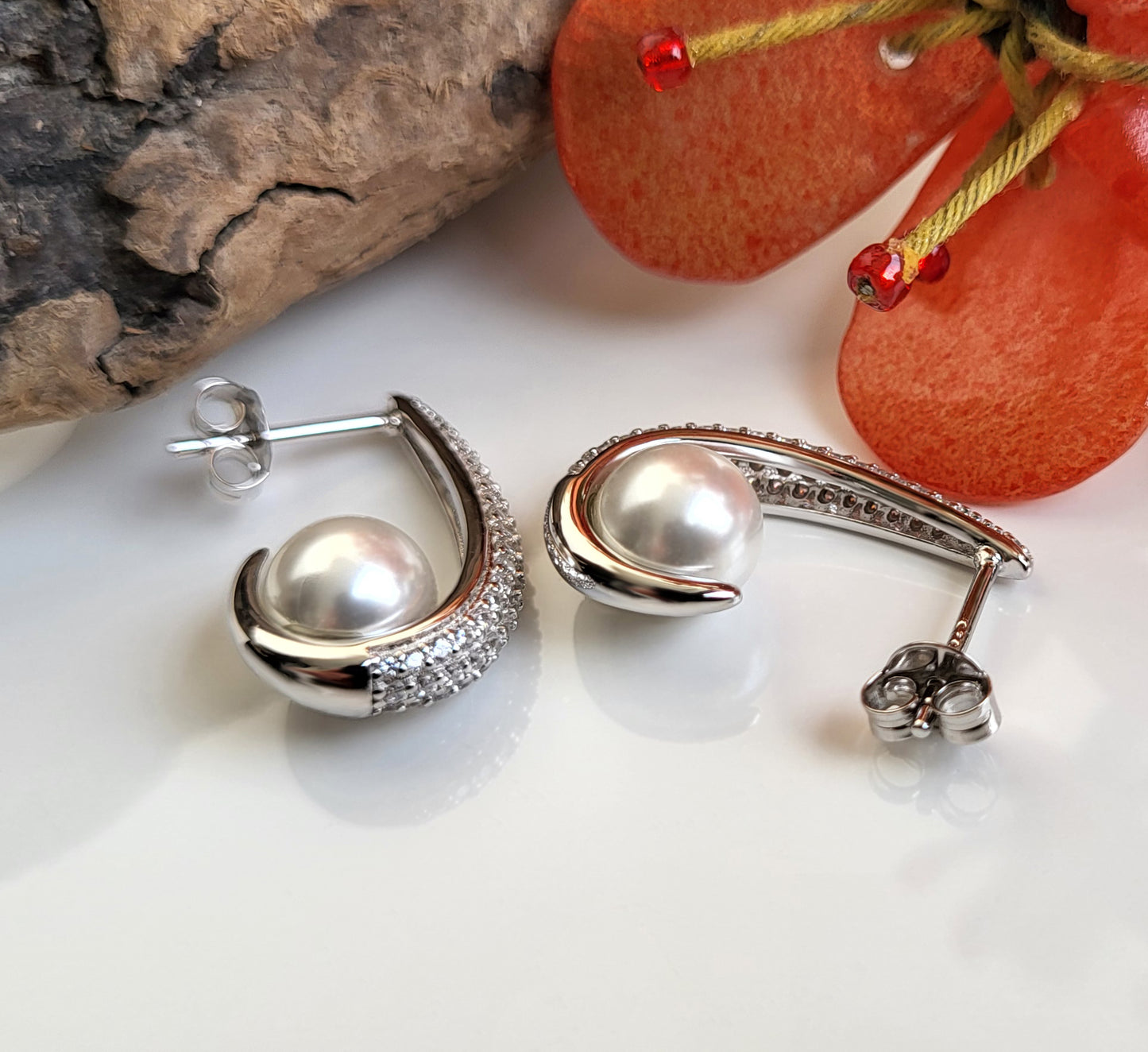 Geschwungene Silberohrringe mit Zirkonia und Perle in liegender Seitenansicht